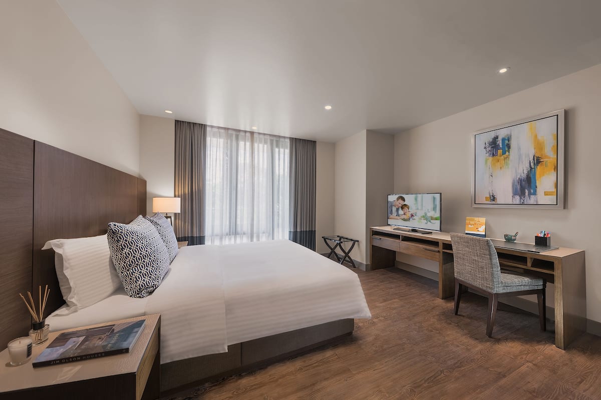 A modern hotel room with a large bed, a desk, and a television.