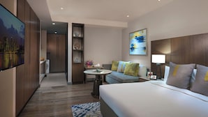 A hotel room with a bed, a sofa, a small table, a TV, and a painting on the wall.
