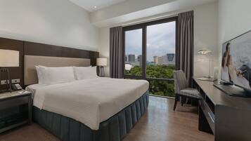 A hotel room with a large bed, a desk with a laptop, a chair, and a TV.