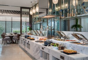 A modern dining area with a marble counter, buffet with various food items, and a seating area with chairs and a table. - Somerset Alabang Manila (Muntinlupa)