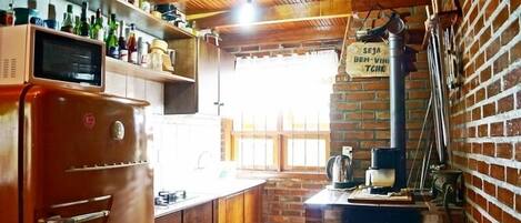 A rustic kitchen with a brick wall, wooden ceiling, and a vintage refrigerator.