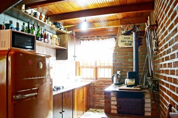 A rustic kitchen with a brick wall, wooden ceiling, and a vintage refrigerator.