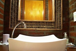A bathroom with a white sink, a mirror with a wooden frame, and a brick wall.