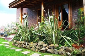 A rustic brick house with a wooden porch, large plants, and a stone pathway. - Chalé 58 (Gramado)