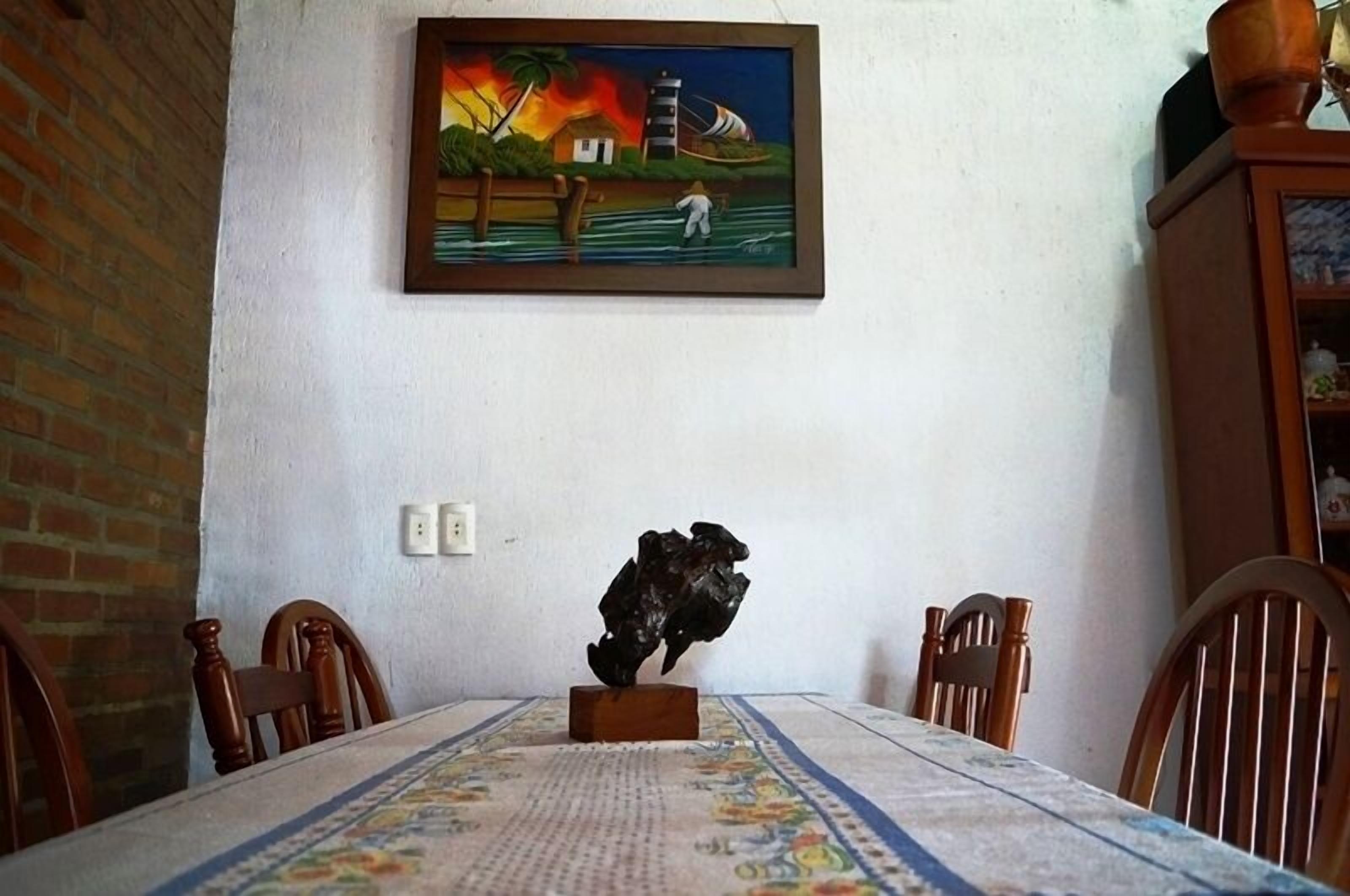 A dining area with a table set for four, a painting above the table, and a small sculpture on the table.
