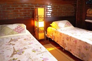 A cozy room with two beds, a brick wall, and a lit lamp.