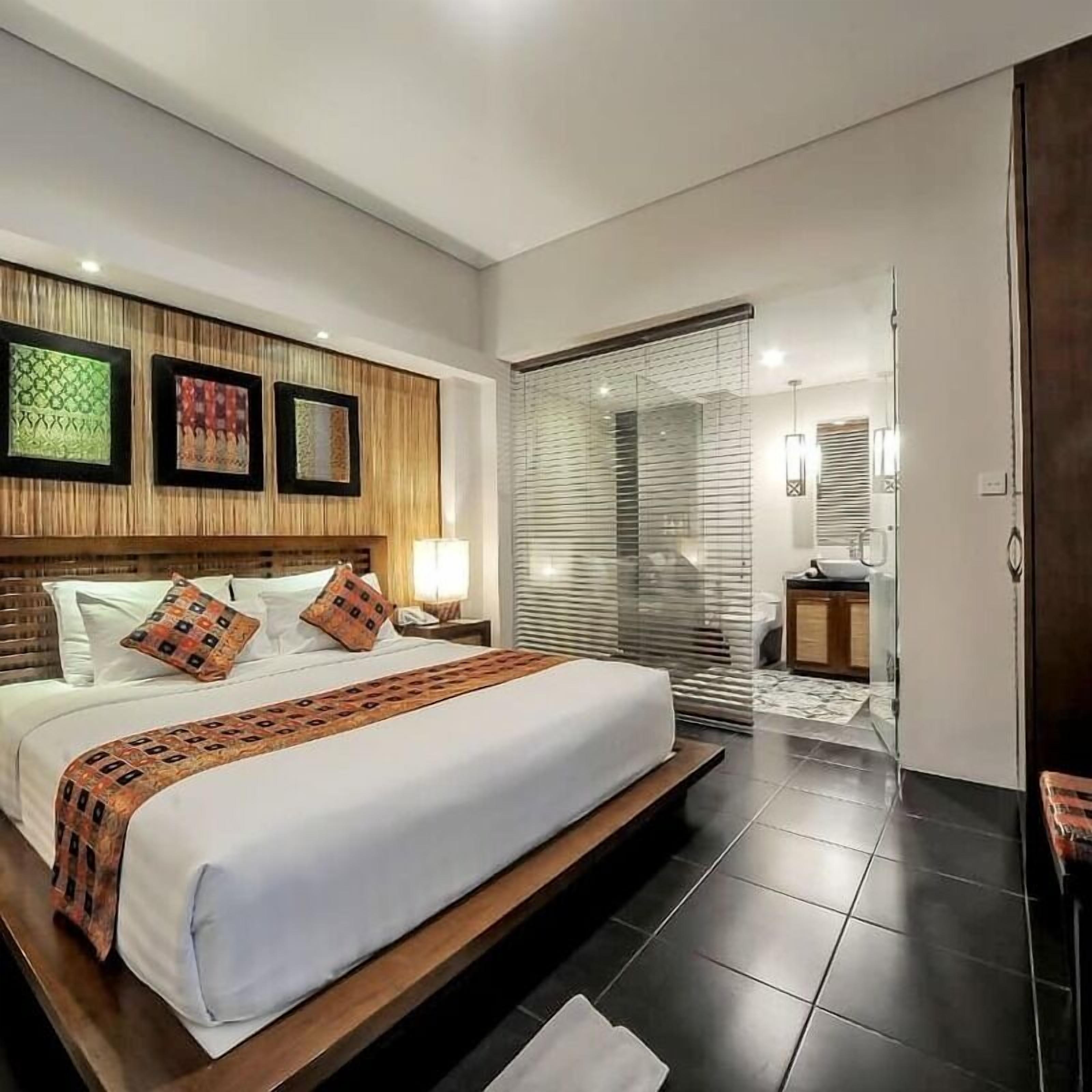 Une chambre d’hôtel moderne avec un grand lit, une tête de lit en bois et une vue à travers une porte vitrée.