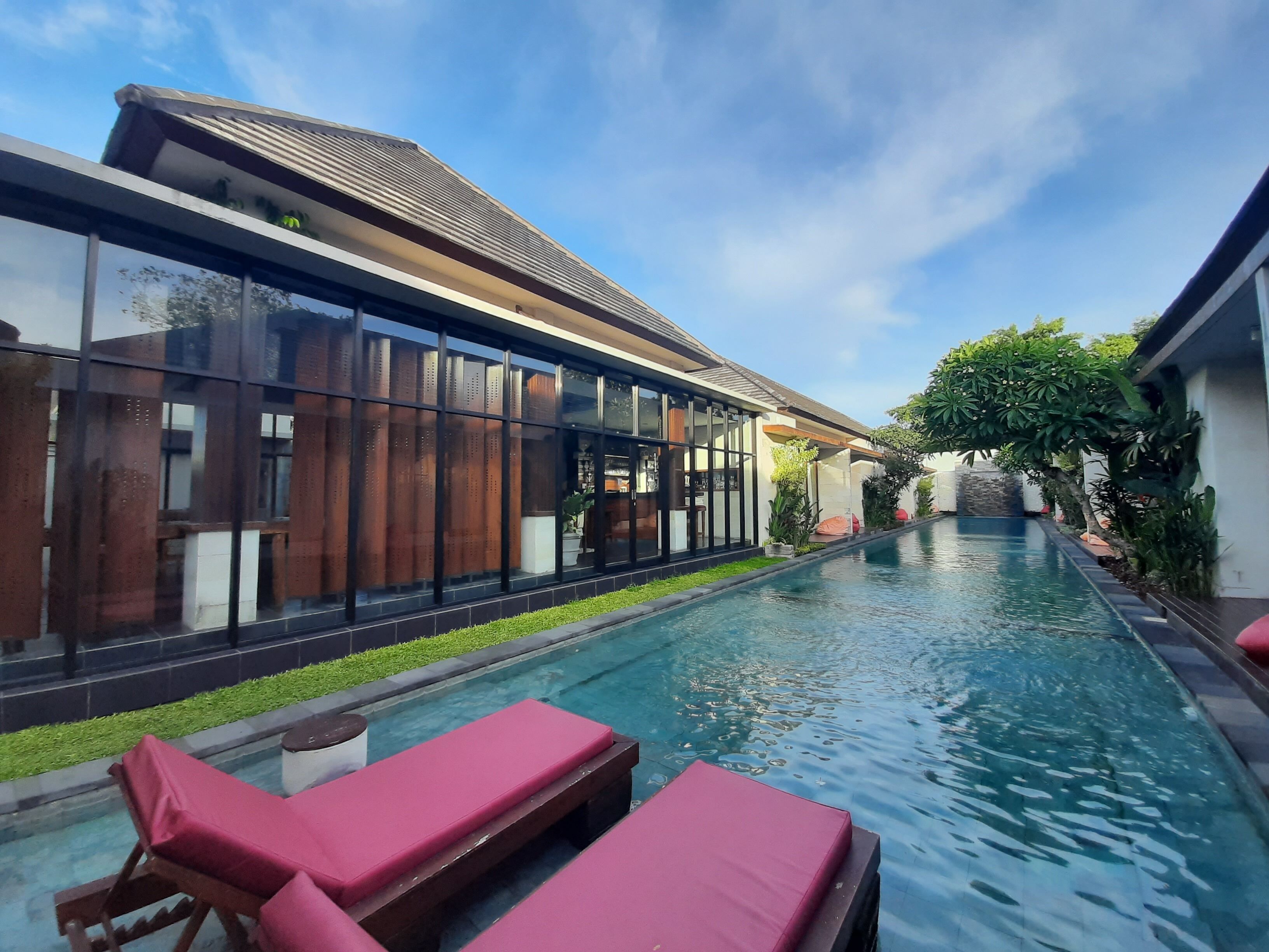 A swimming pool with lounge chairs, a modern building with large windows, and a clear sky.