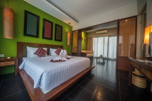 Una habitación de hotel amplia con una cama grande, un cabecero de madera, un pequeño rincón de descanso y vistas a la ciudad a través de amplias ventanas.