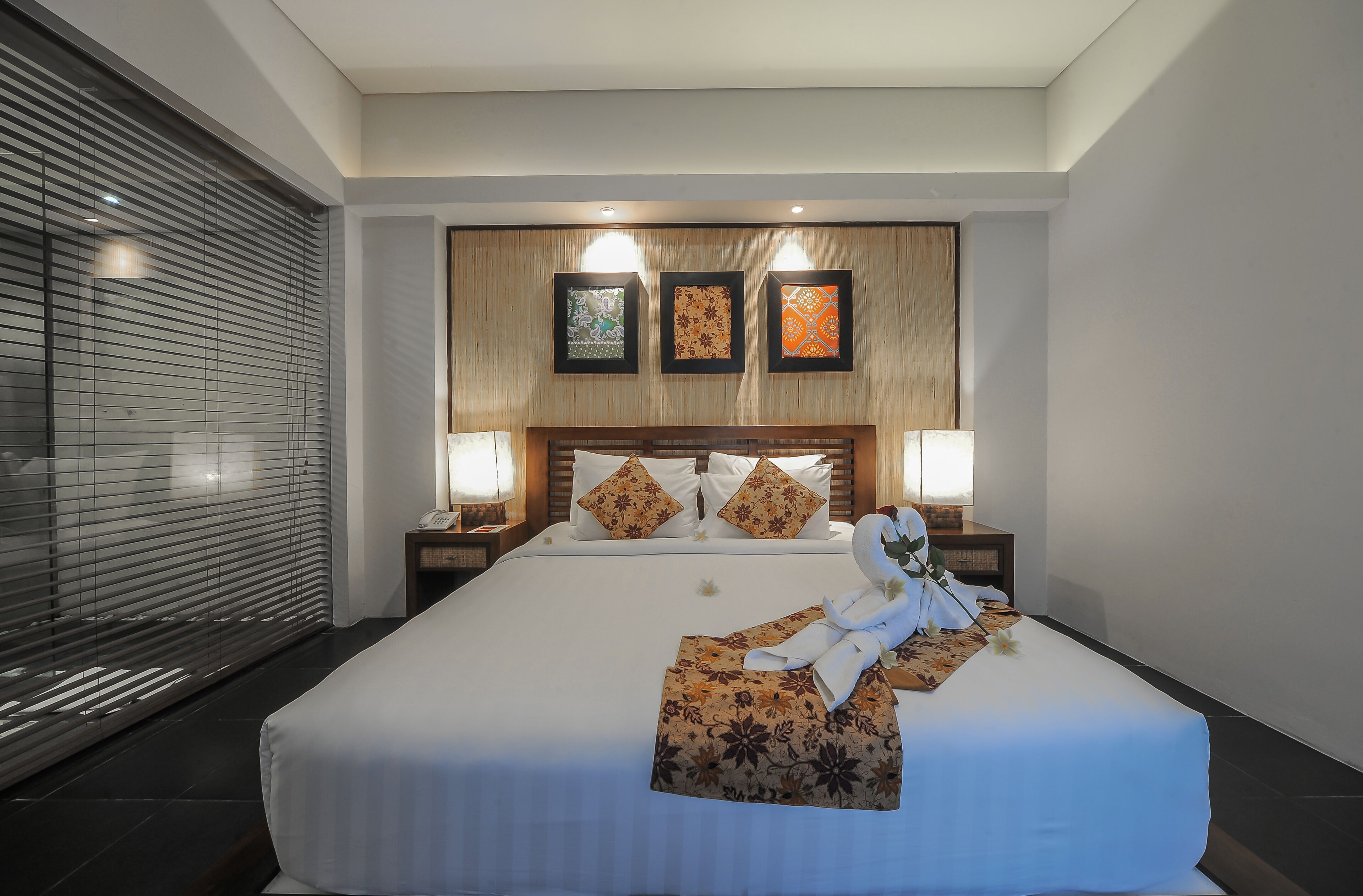 Una habitación de hotel con una cama grande, dos mesitas de noche, un cabecero de madera y tres lámparas fijadas a la pared.