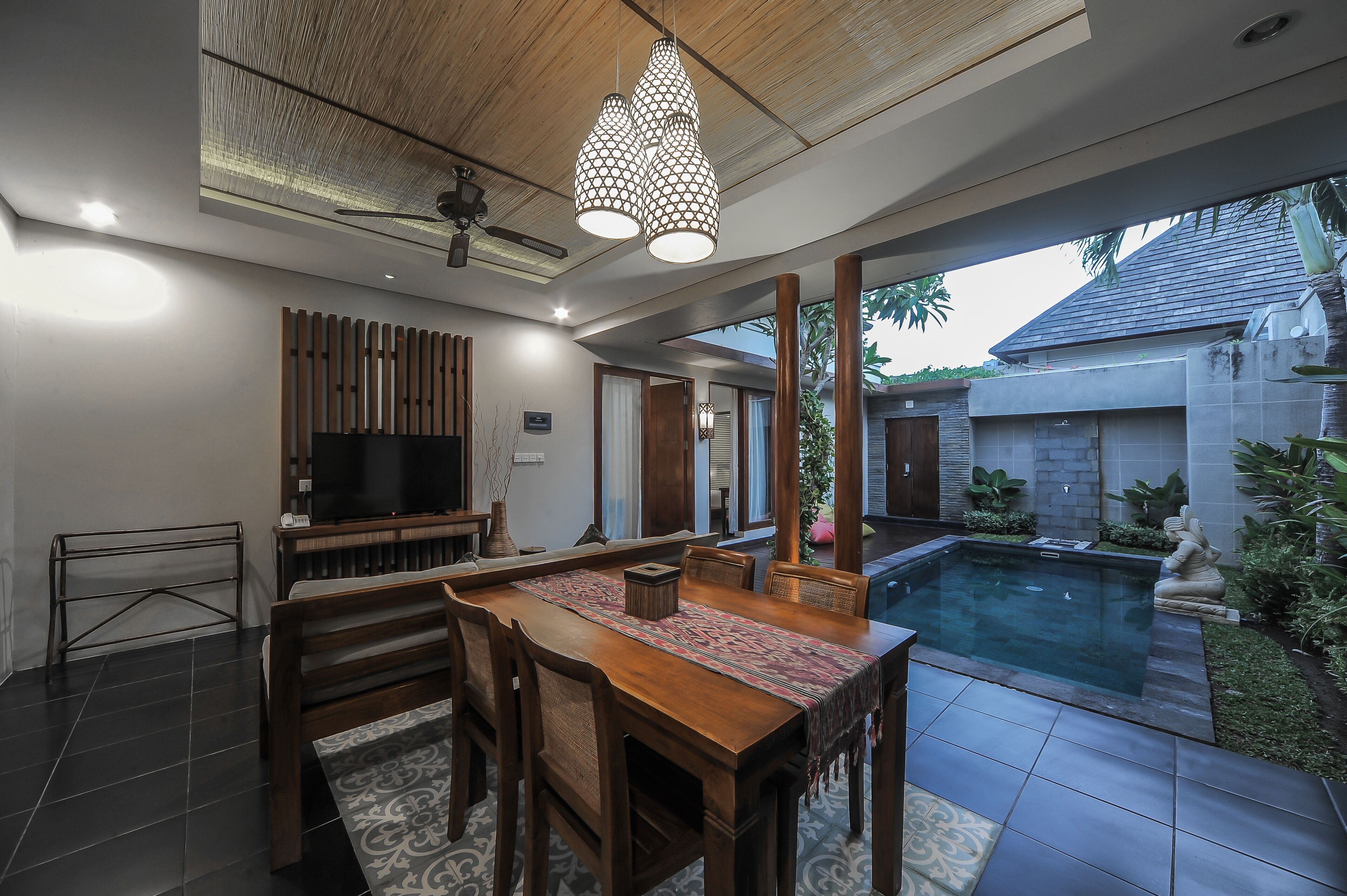 Un salon moderne avec un téléviseur, des meubles en bois, un tapis à motifs et une vue sur une piscine.