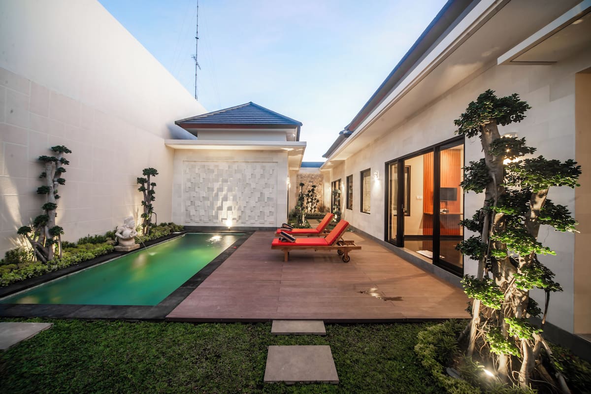 A modern outdoor pool area with two red lounge chairs, a small pool, and a well-maintained garden.