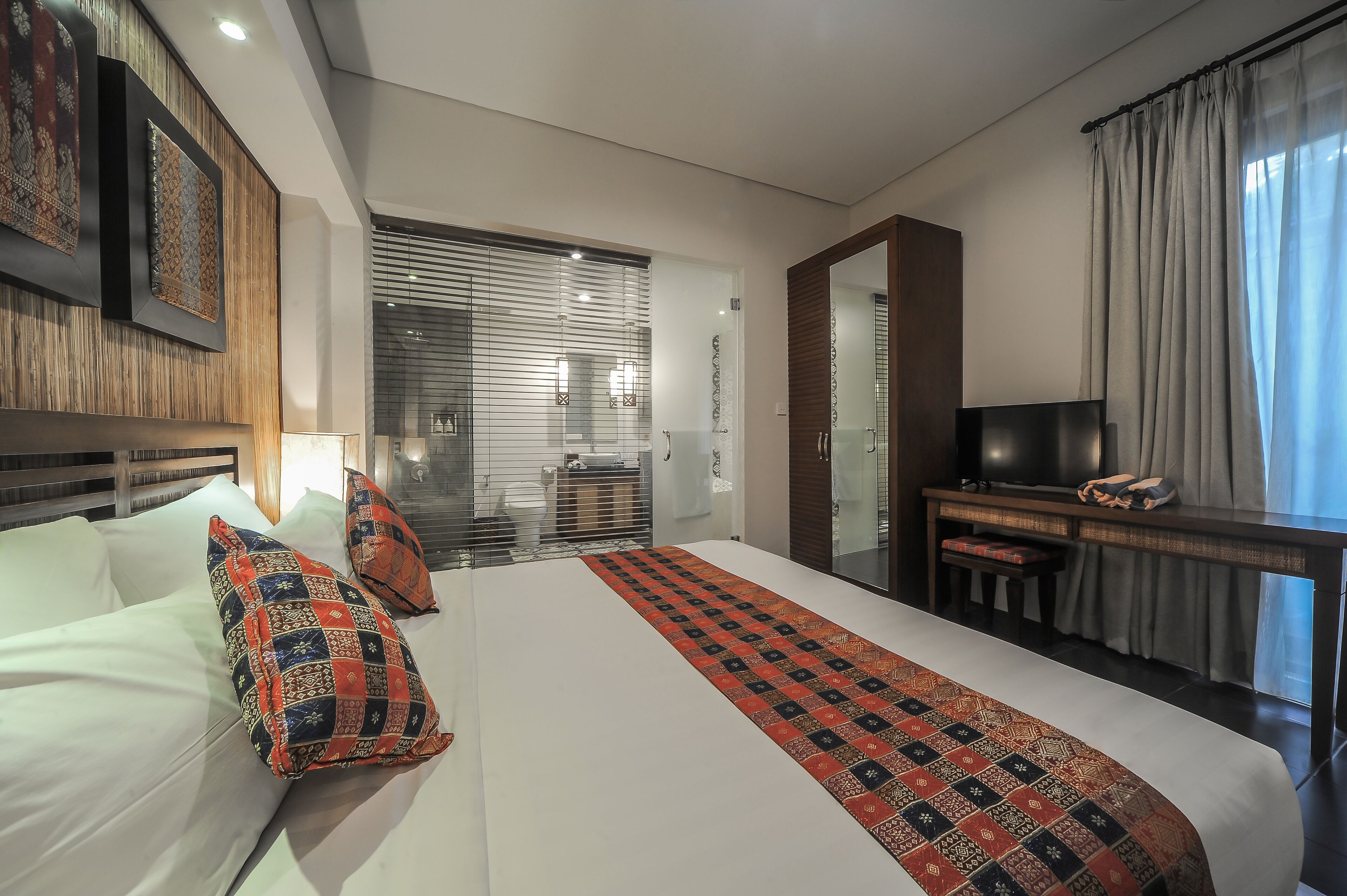 A hotel room with a large bed, a desk with a chair, a television, and a wardrobe.