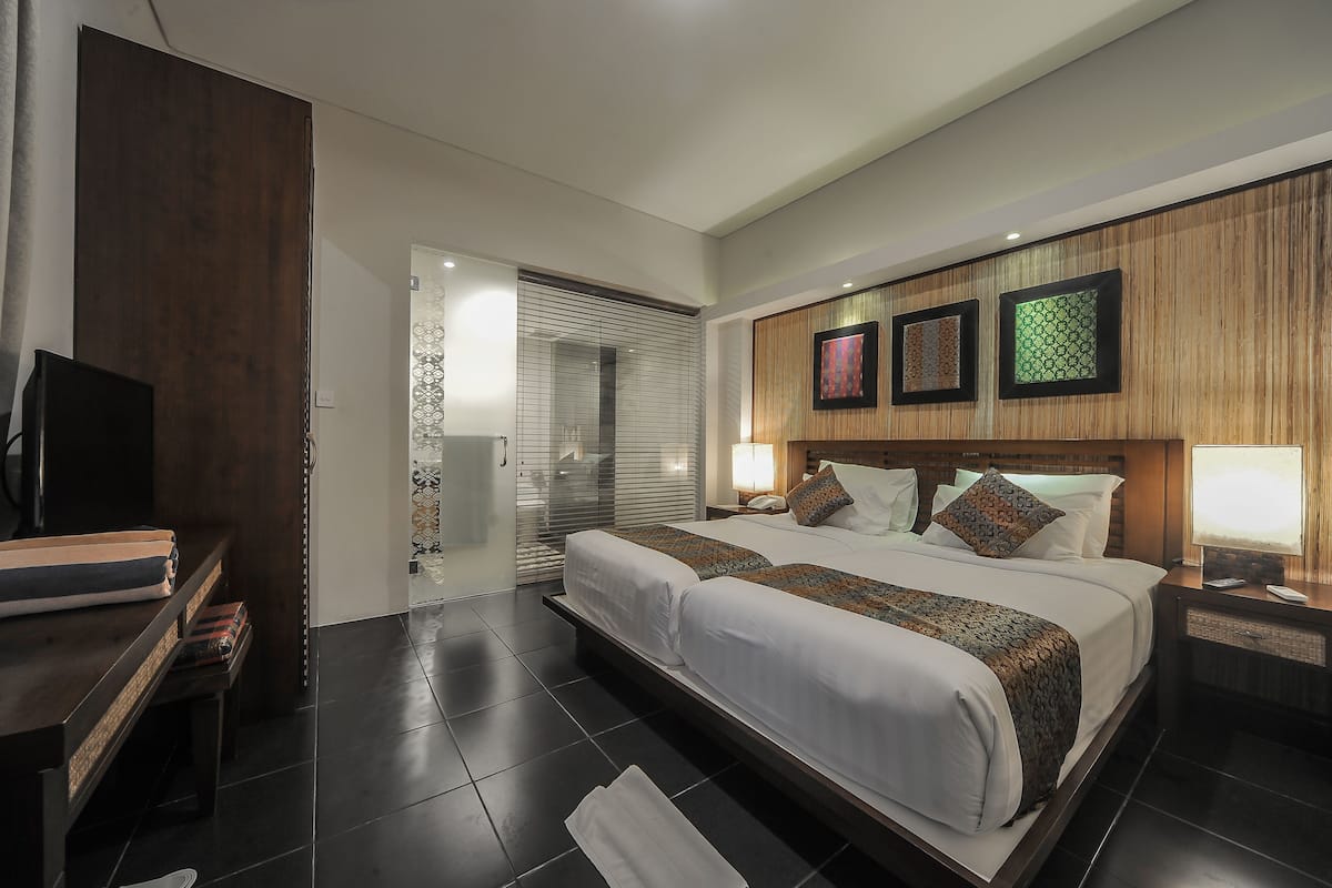 A modern hotel room with a large bed, a television, a desk, and a bathroom with a glass door.