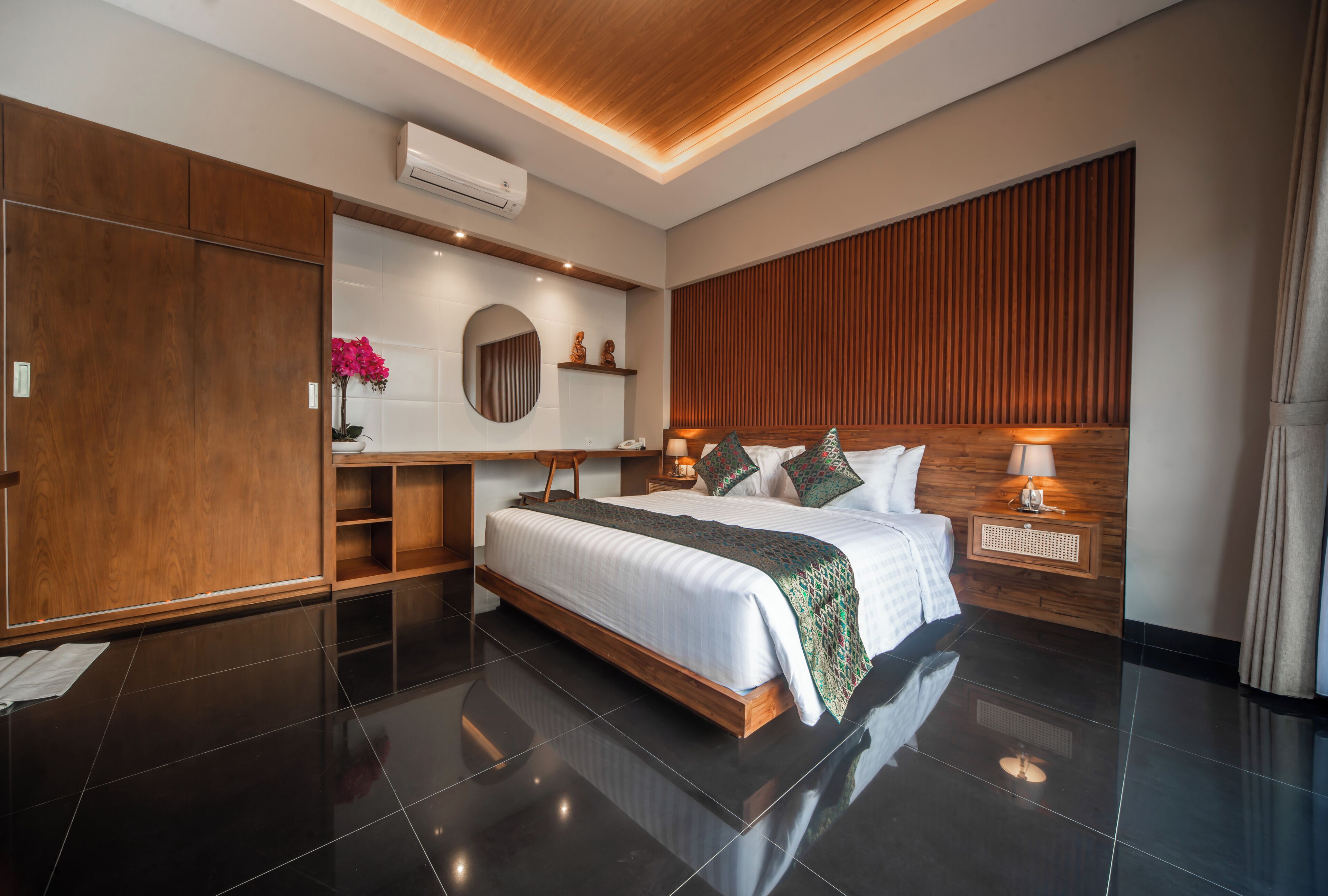 A modern bedroom with a large bed, wooden paneling, a vanity with a mirror, and a nightstand with a lamp.