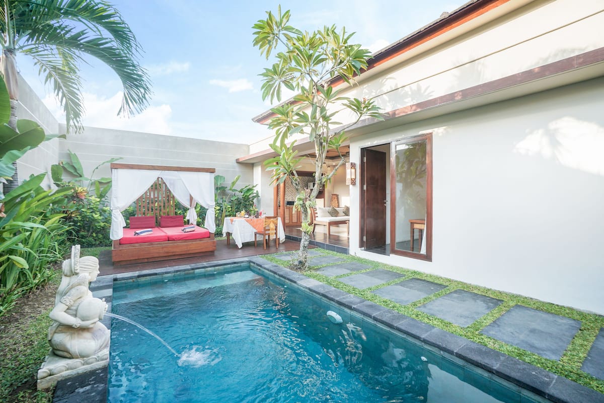 A private pool with a statue, a red sofa, and a dining area with a table and chairs.