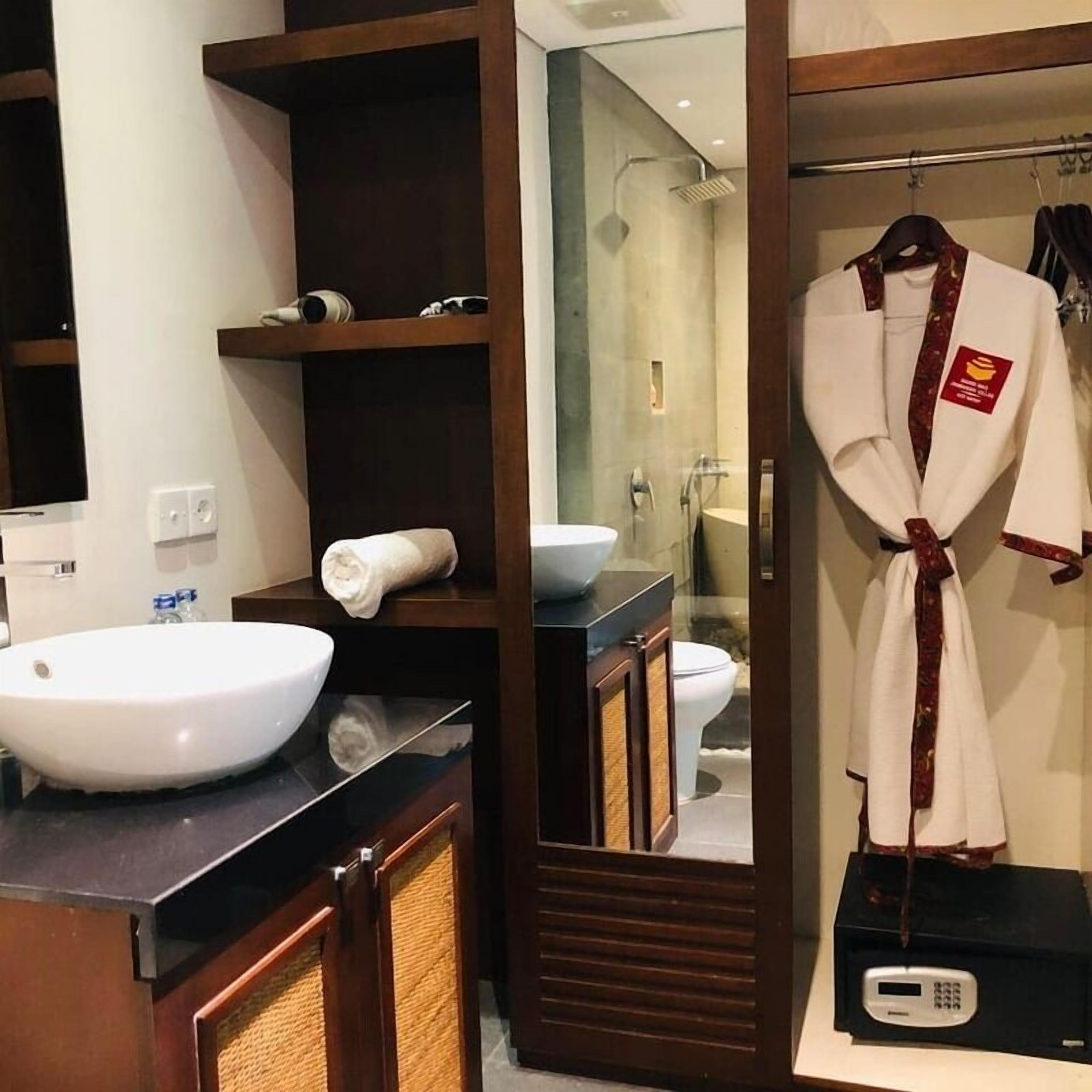 A bathroom with a large white sink, a mirror, a towel, and a robe hanging on a rack.