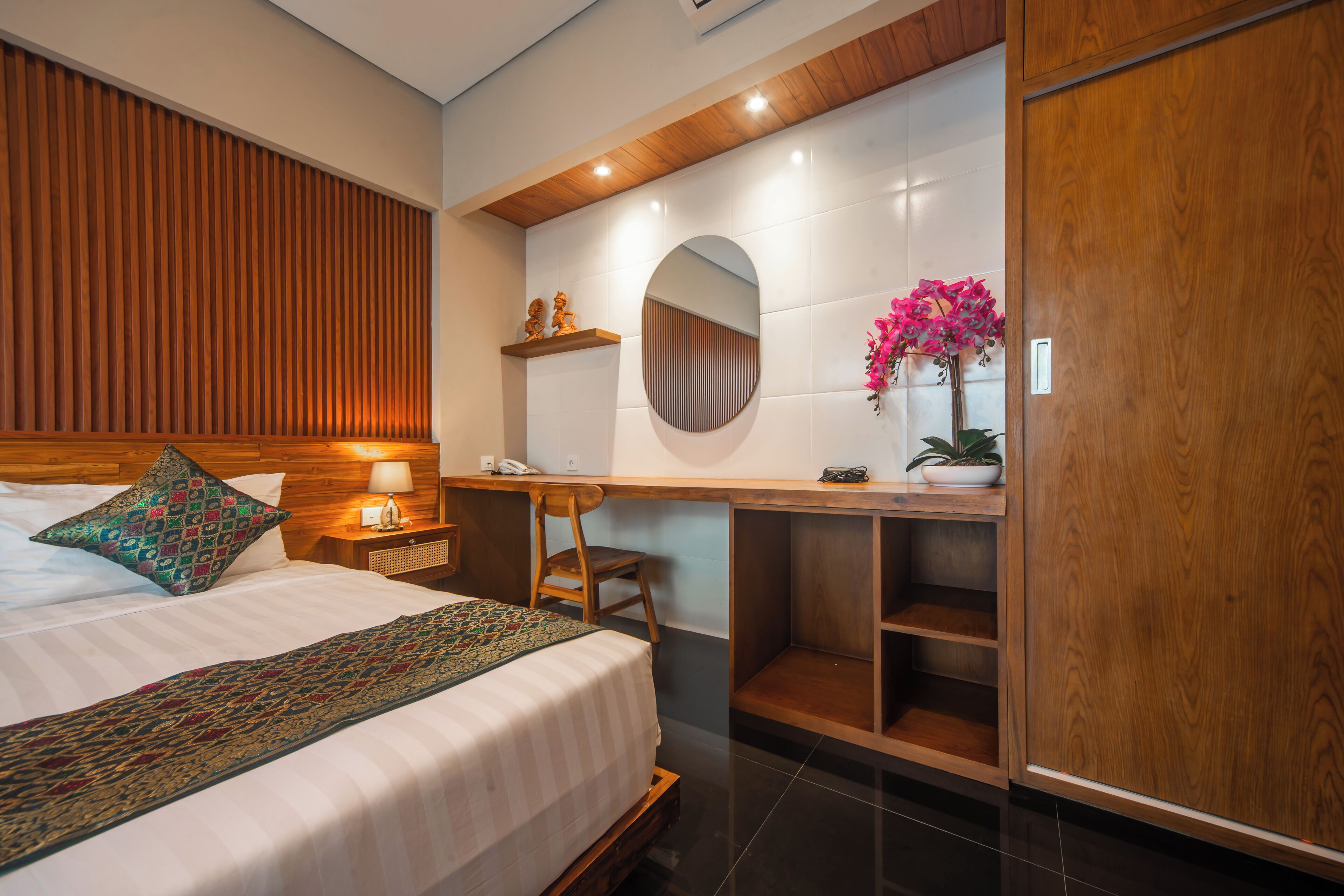 A modern hotel room with a large bed, a wooden desk, a mirror, and a potted plant.