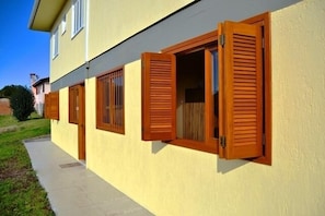 A two-story building with a yellow exterior and wooden shutters on the windows. - Residencial Daniel (Gramado)