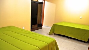 Una habitación con dos camas cubiertas con ropa de cama verde, un armario de madera y un piso de baldosas de color claro.