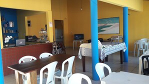 A dining area with a counter, white plastic chairs, a wooden table, and a painting on the wall.