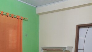 A bedroom with two beds, a green wall, an orange curtain, and a white door.