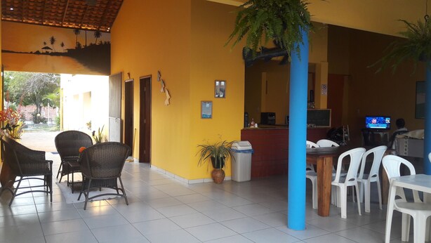 A hotel lobby with wicker chairs, a reception desk, a television, and a potted plant.