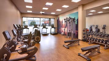 Un gimnasio con máquinas de cardio, bancos de pesas y pesas libres.
