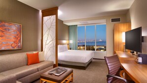 Ein Hotelzimmer mit Bett, einer Couch, einem Schreibtisch und Blick auf die Stadtlandschaft.