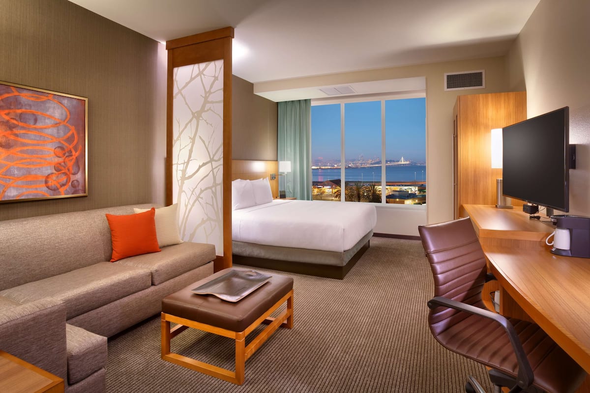 Habitación de hotel con cama, sofá, escritorio y vistas a la ciudad.