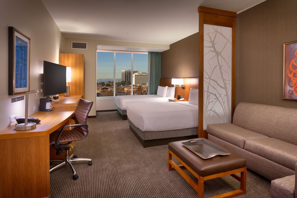 Habitación de hotel con escritorio, dos camas, un sofá y vistas a la ciudad.