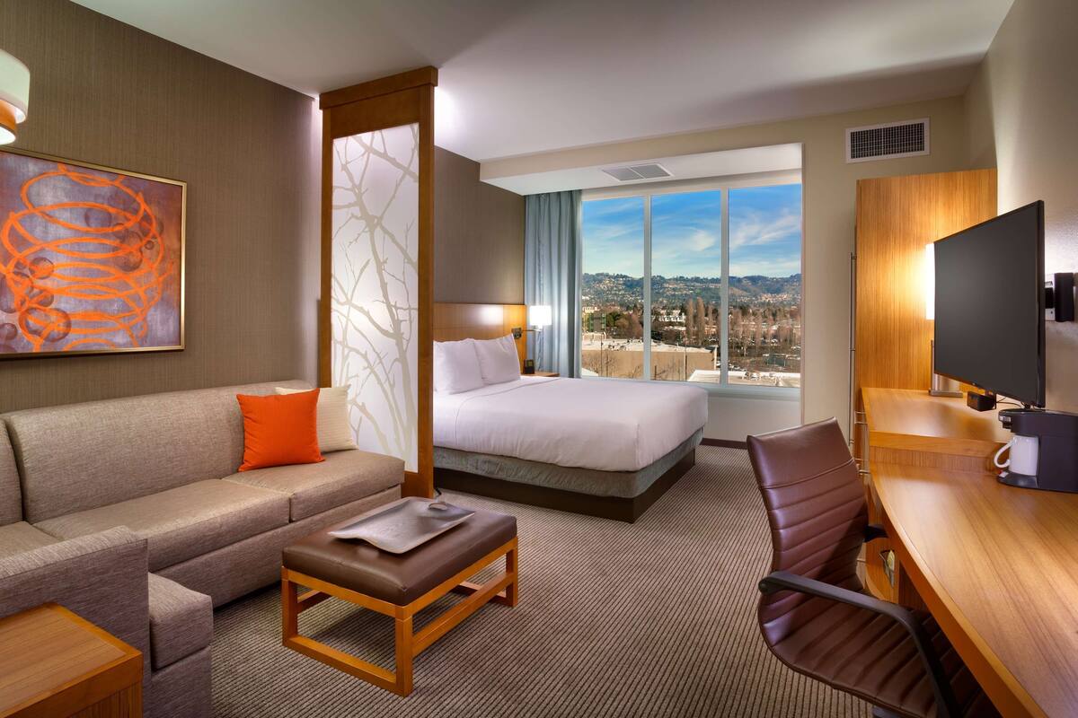 Habitación de hotel con cama, sofá, escritorio y vistas a la ciudad.