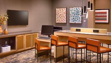 A hotel room with a desk, two monitors, a printer, and a seating area with chairs.