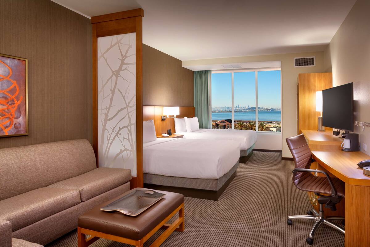 Habitación de hotel con una cama grande, un sofá, un escritorio y vistas a la ciudad.