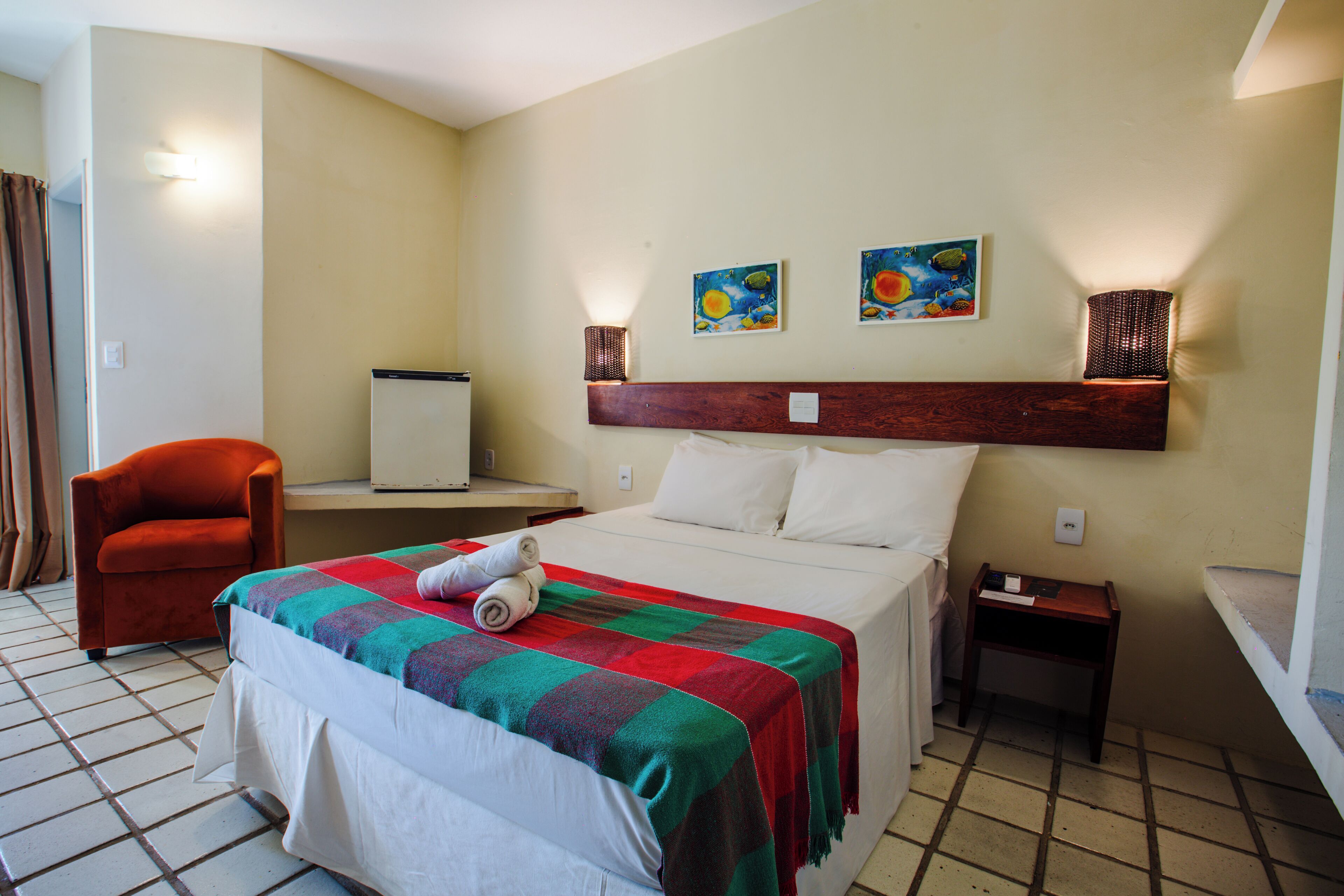 A hotel room with a bed, a chair, a nightstand, and two wall-mounted lamps.