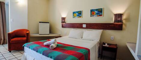 A hotel room with a bed, a chair, a nightstand, and two wall-mounted lamps.