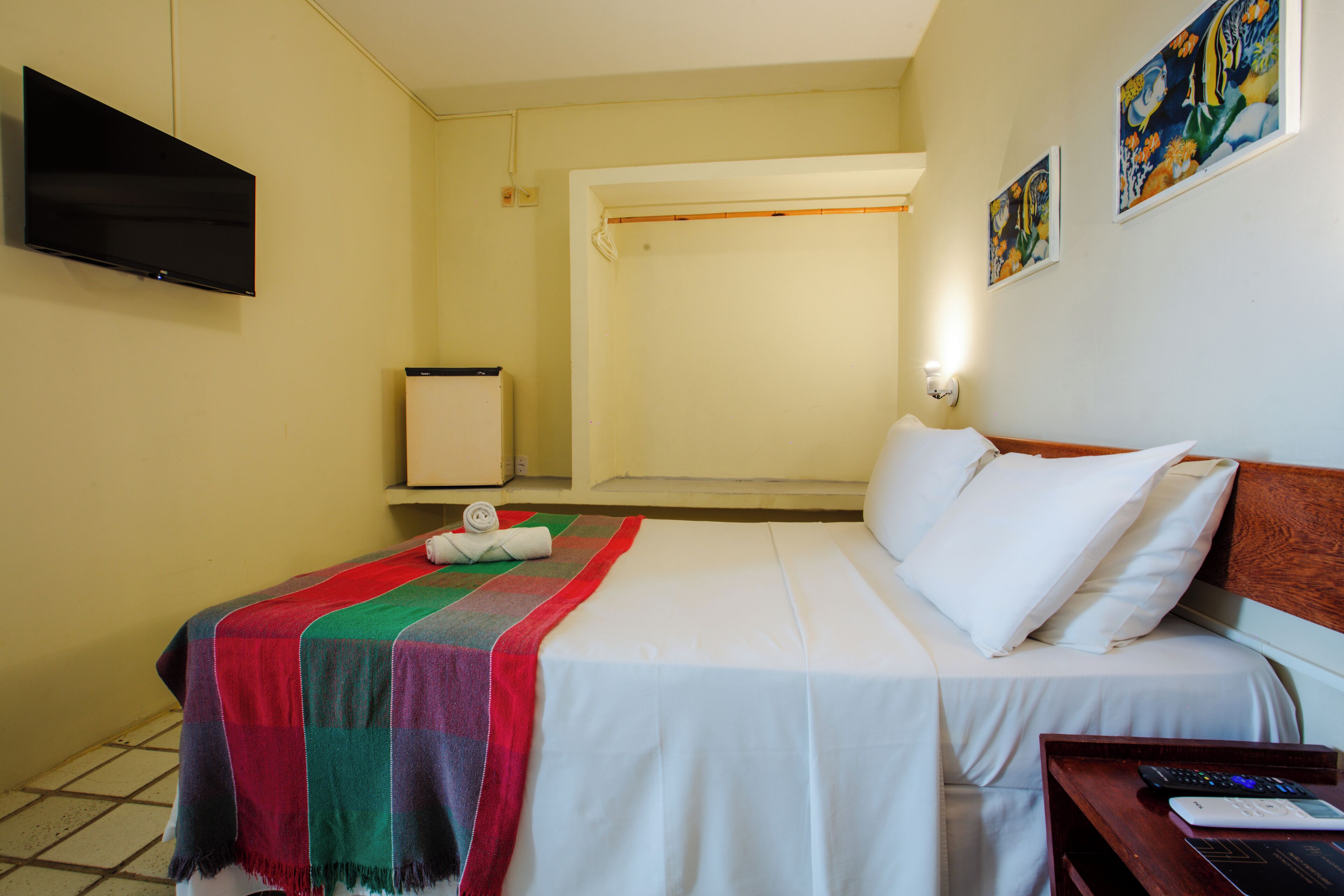 A hotel room with a bed, a television mounted on the wall, and artwork on the wall.