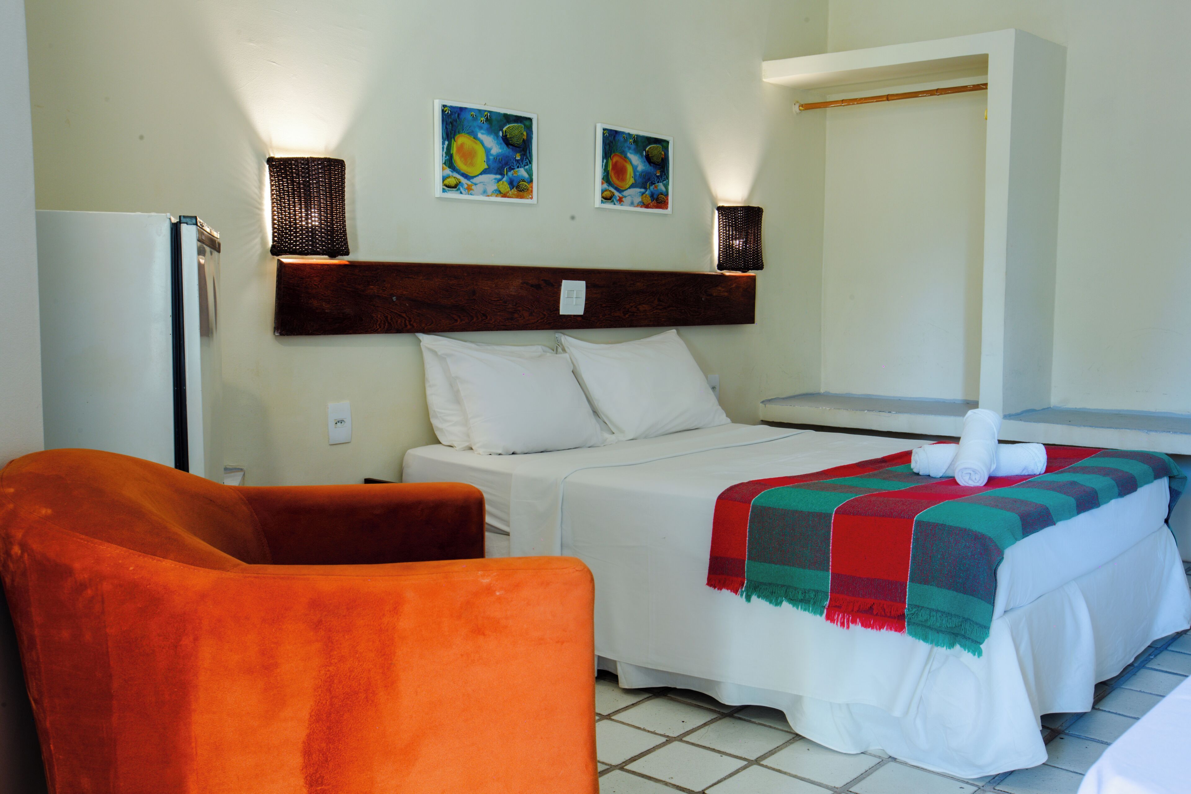 A hotel room with a bed, a chair, and a wall-mounted lamp.