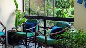 Una habitación con tres sillas de mimbre con cojines verdes, un ventanal con vistas a la vegetación y un suelo de baldosas.