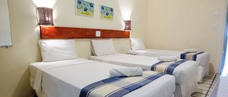 A hotel room with four single beds, each with a white mattress and a blue and white striped blanket. There are two wall-mounted lamps on either side of the headboard, and two paintings above the beds.