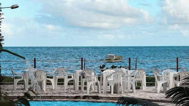 Zona junto a la piscina con sillas de plástico blancas y vista al mar.