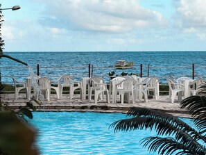 Zona junto a la piscina con sillas de plástico blancas y vista al mar.