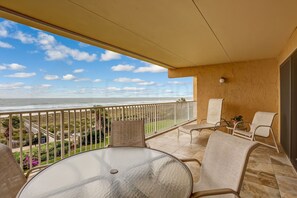 A balcony with a glass table and chairs, overlooking a beach with a railing and greenery. - Oceanfront Condo with Spacious Patio and Private Walkway to the Beach by RedAwning (Fernandina Beach)