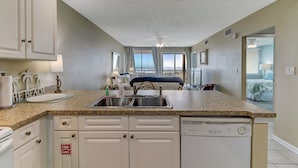 A compact kitchen with a dishwasher, a sink, and a ceiling fan. - Coral Sands 102 2 Br condo by RedAwning (Fernandina Beach)