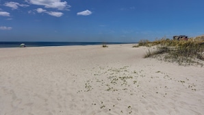 A sandy beach with a clear sky and a few clouds. There are some plants on the sand and a structure in the background. - Coral Sands 102 2 Br condo by RedAwning (Fernandina Beach)