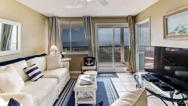 A living room with a white sofa, a television, a ceiling fan, and a view of the outdoors. - Coral Sands 102 2 Br condo by RedAwning (Fernandina Beach)