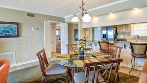 A dining area with a glass table, wicker chairs, and a hanging light fixture. - Oceanfront Condo, Private Walkway to the Beach by RedAwning (Fernandina Beach)