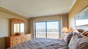 A hotel room with a large bed, a dresser, a mirror, a window with a view, and a lamp. - Oceanfront Condo, Private Walkway to the Beach by RedAwning (Fernandina Beach)