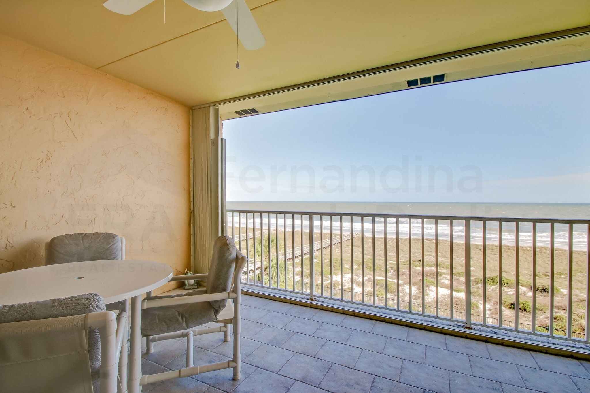 A balcony with a view of the beach, a round table, and two chairs.