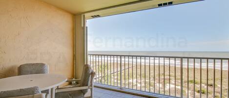 A balcony with a view of the beach, a round table, and two chairs.